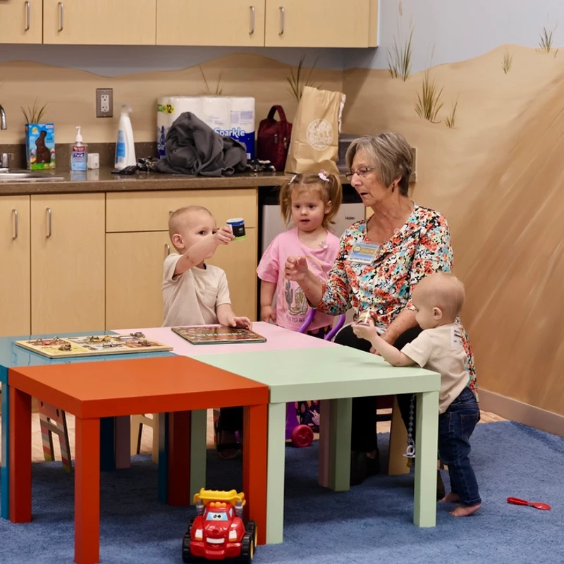 A caregiver plays with toddlers at a colorful play table in a nursery classroom at The Crossing in Milton, DE.